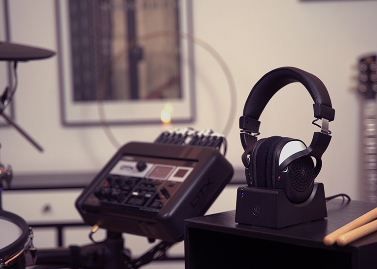 DTX drum module in soft focus. Drum sticks & YH-WL500 in charging dock on top of a home desk.