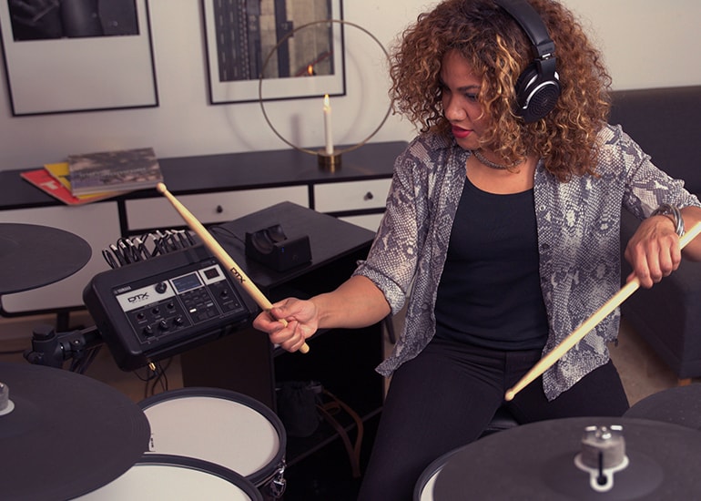 Drummer playing DTX electronic drum kit while wearing YH-WL500 headphones in a home setting.