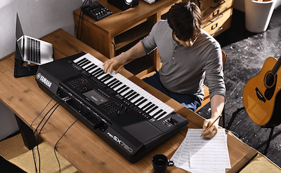 Photo of a person writing on sheet music while playing the Yamaha Arranger Workstation PSR-SX720